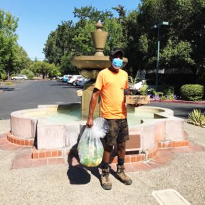 Person standing by a water fountain holding a bag of vegetables